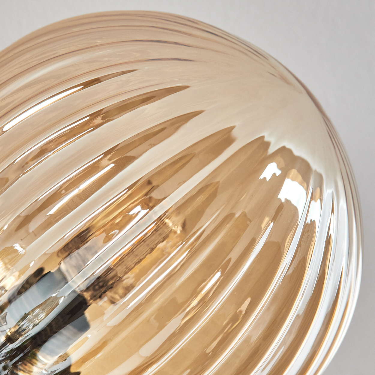 Nahaufnahme einer bernsteinfarbenen Glaskugel mit gerippter Textur, die Licht reflektiert.