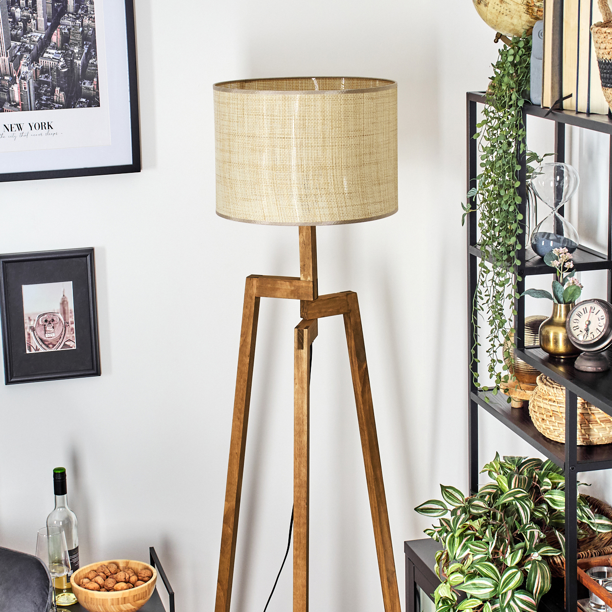 Holz-Stativ-Stehlampe mit beigem Lampenschirm. Bücher, Deko und ein Gemälde im Hintergrund.