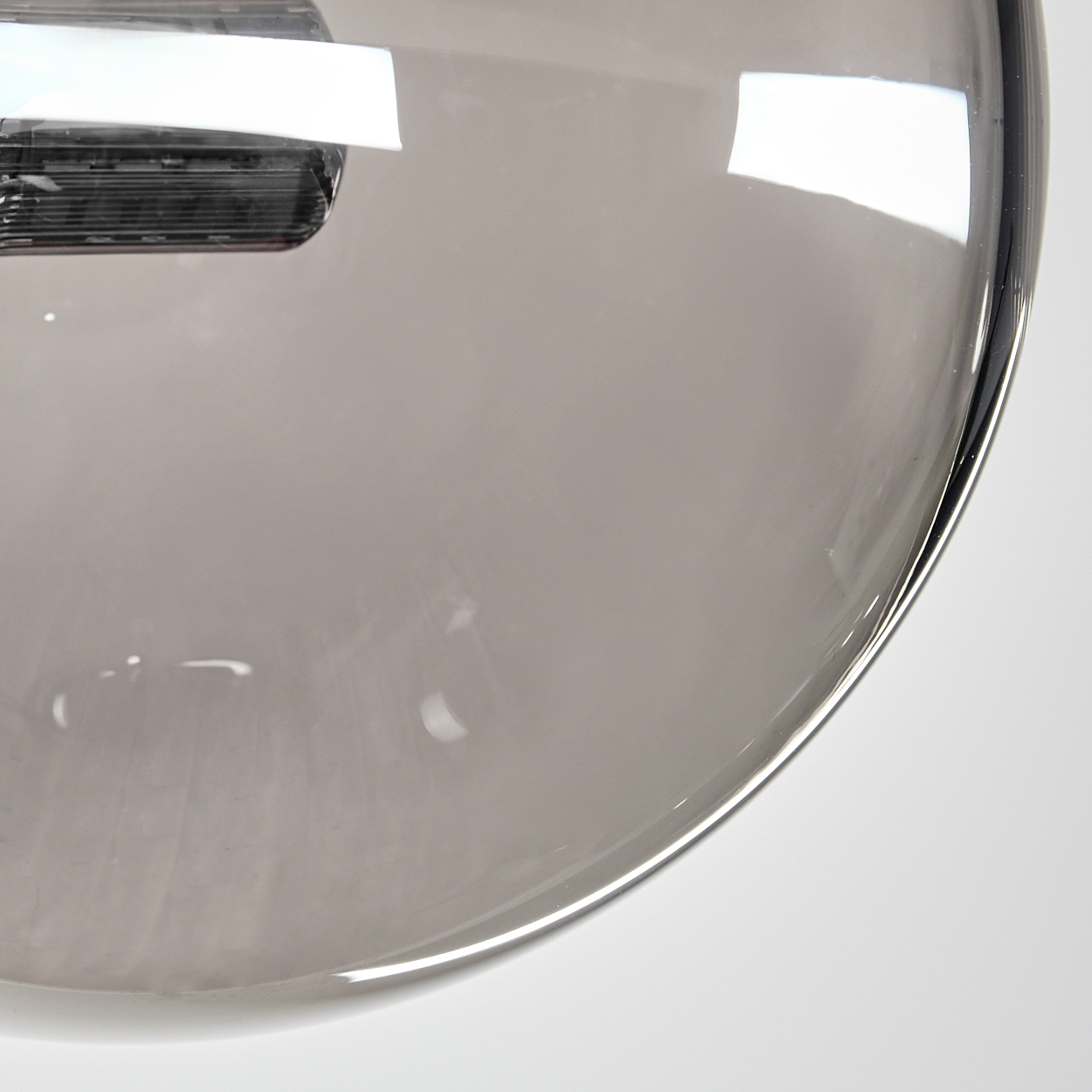 Nahaufnahme einer reflektierenden, grauen Glaskugel mit gebogenem Rand. Weißer Hintergrund.