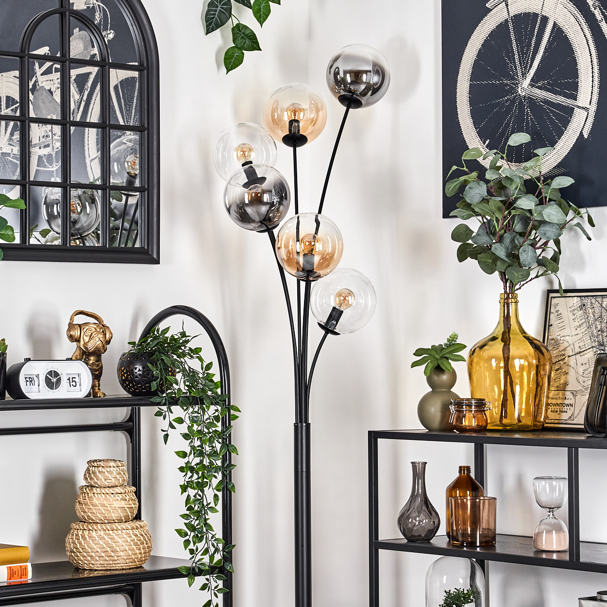 Wohnzimmerdekoration. Schwarze Regale, Pflanzen, Dekorationsartikel und eine Stehlampe mit mehreren Glaskugelschirmen.