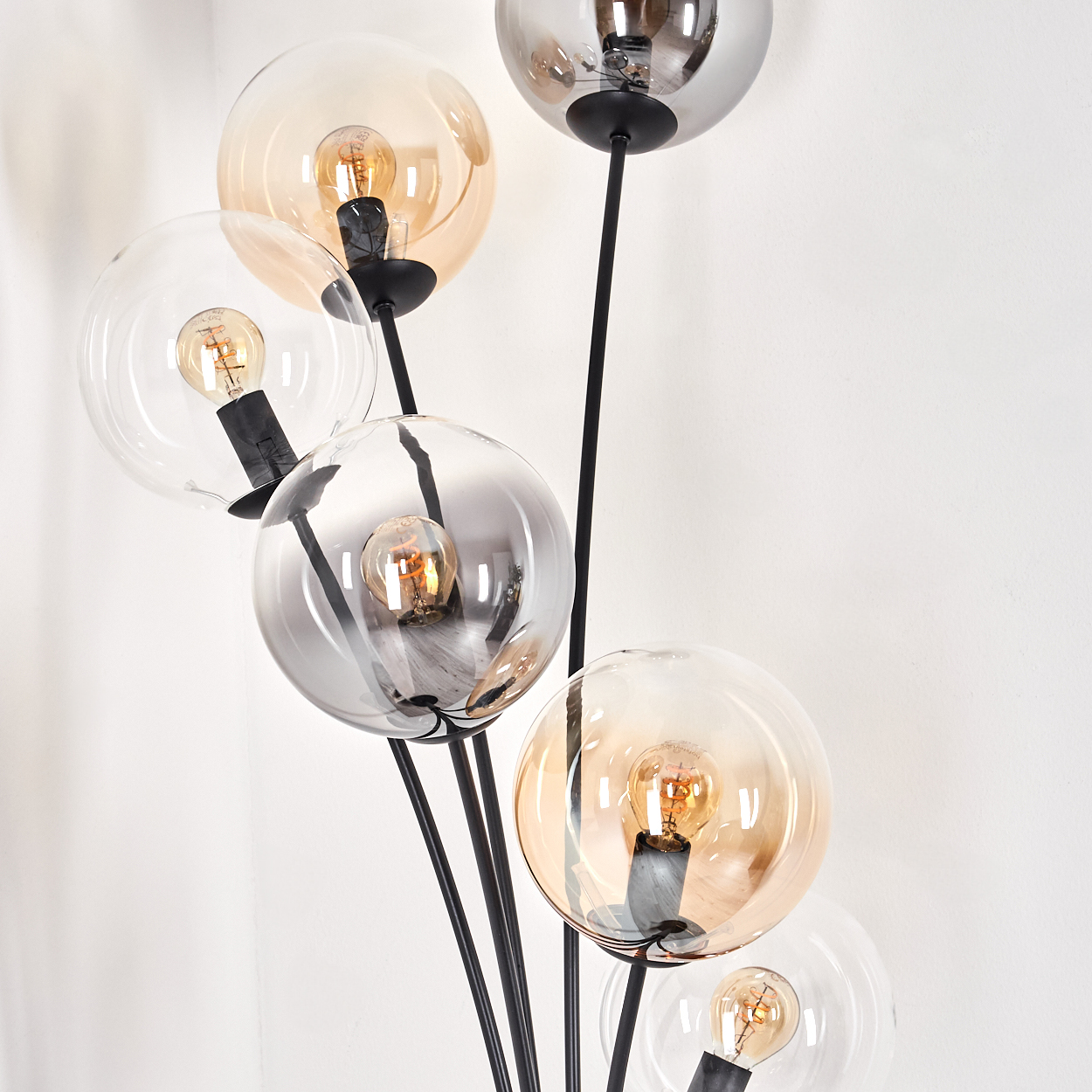Nahaufnahme einer Stehlampe. Mehrere kugelförmige Glasschirme mit freiliegenden Glühbirnen. Schwarzer Metallrahmen.