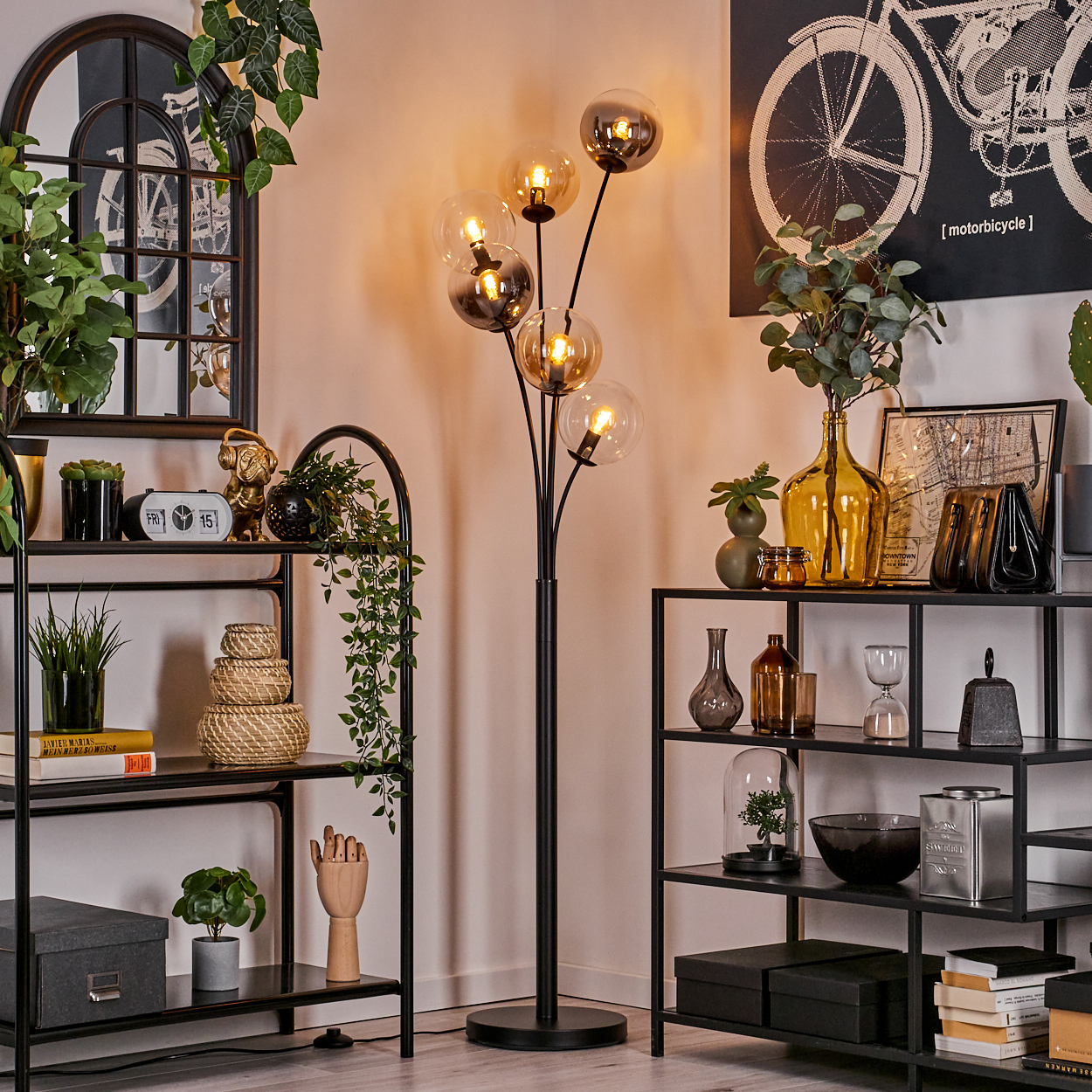 Wohnzimmerszene mit Stehlampe, Regalen, Pflanzen und Dekorationsartikeln. Die Lampe hat Glaskugeln.