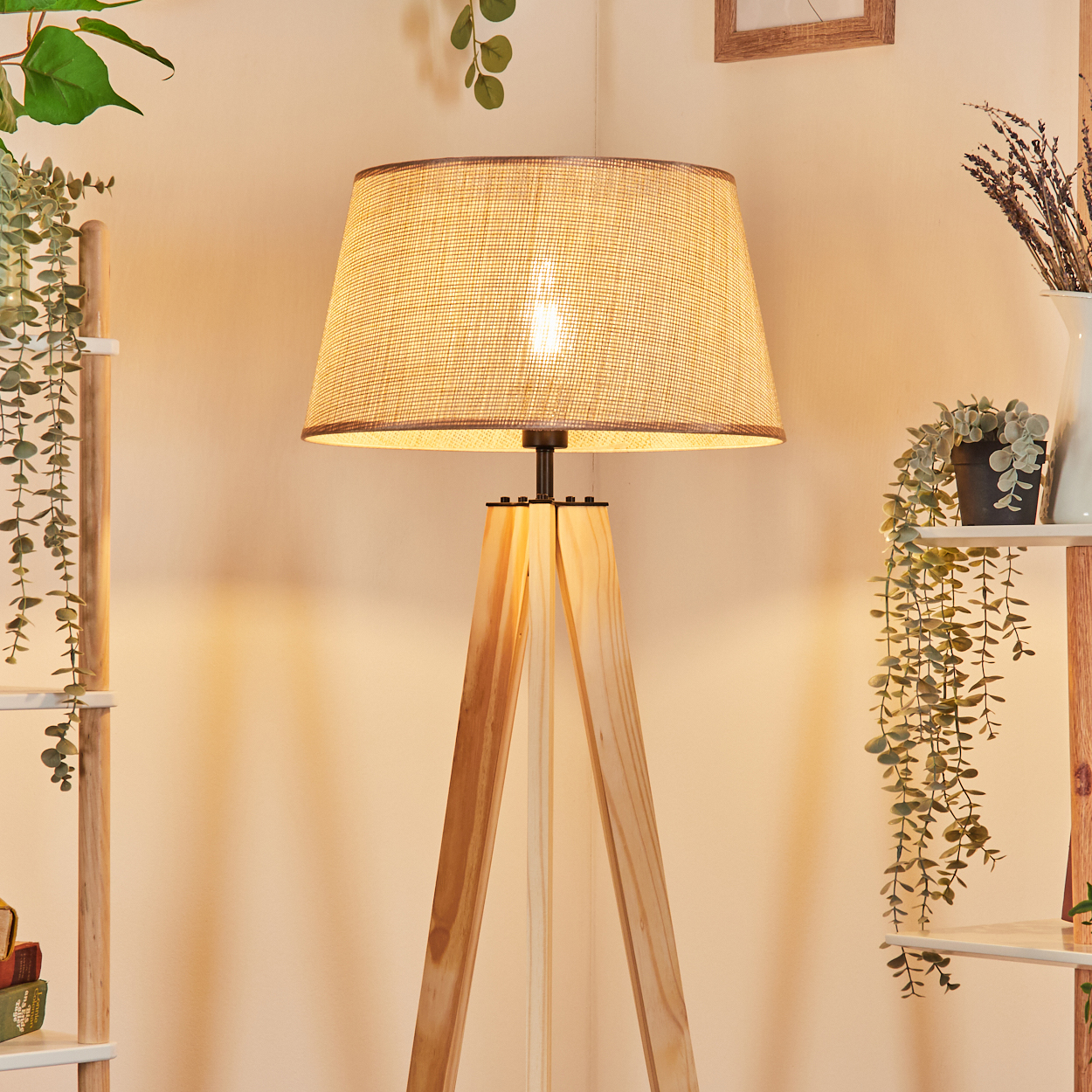 Eine hölzerne Stativ-Stehlampe mit Stoffschirm. Die Szene ist mit einem warmen Schein beleuchtet.