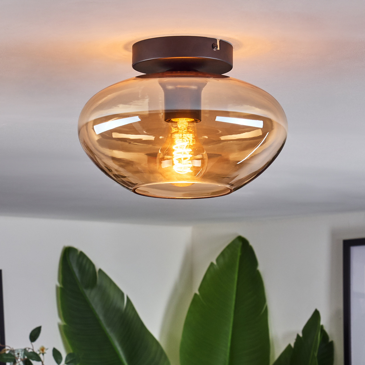 Deckenlampe aus bernsteinfarbenem Glas mit sichtbarer Glühbirne. Weiße Decke.