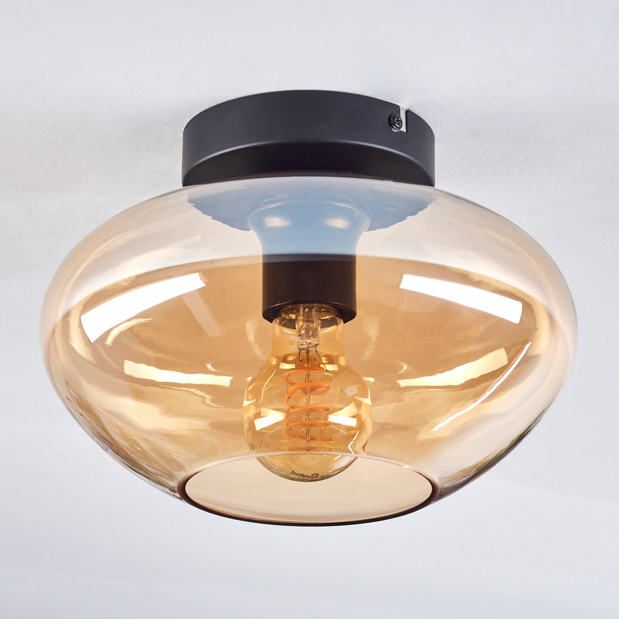 Deckenlampe aus bernsteinfarbenem Glas mit sichtbarer Glühbirne. Weiße Decke.