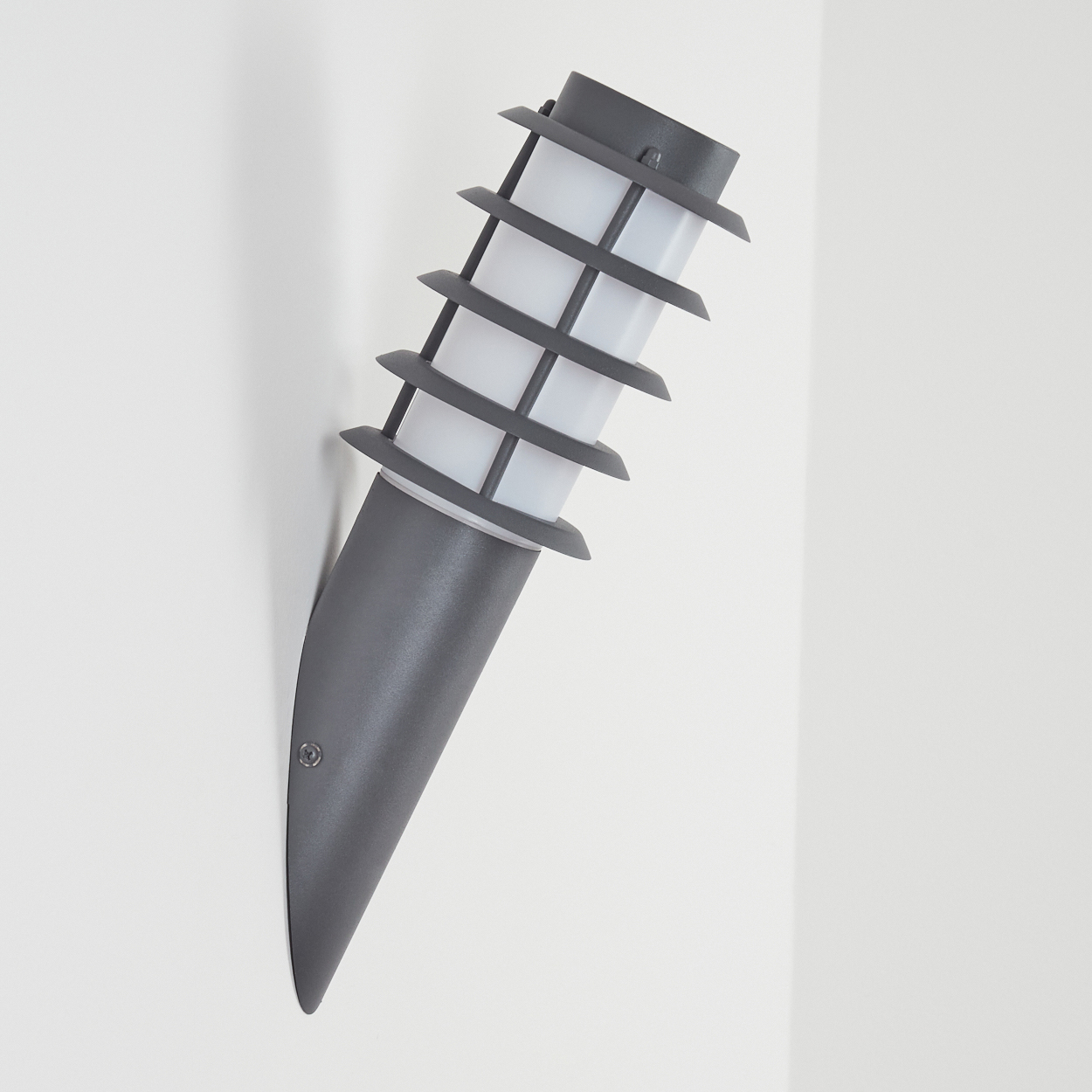 Graue Außenwandleuchte. Weiße Wand. Die Lampe hat weißes Licht.