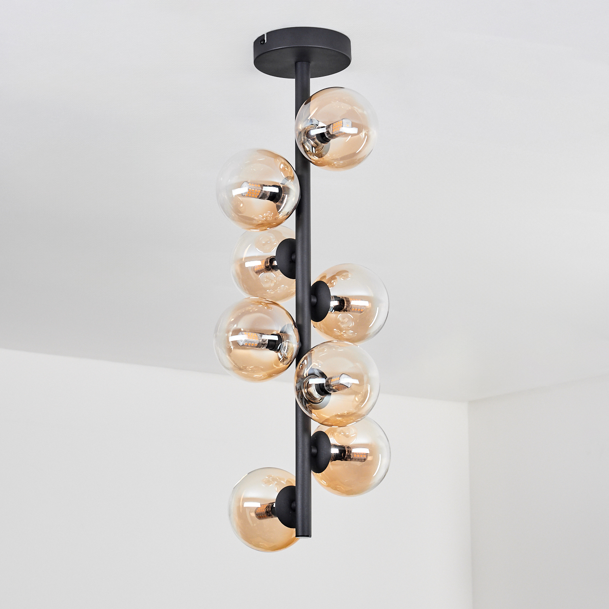 Schwarze Metalllampe mit 8 bernsteinfarbenen Glaskugelschirmen. Deckenmontage. Weißer Hintergrund.