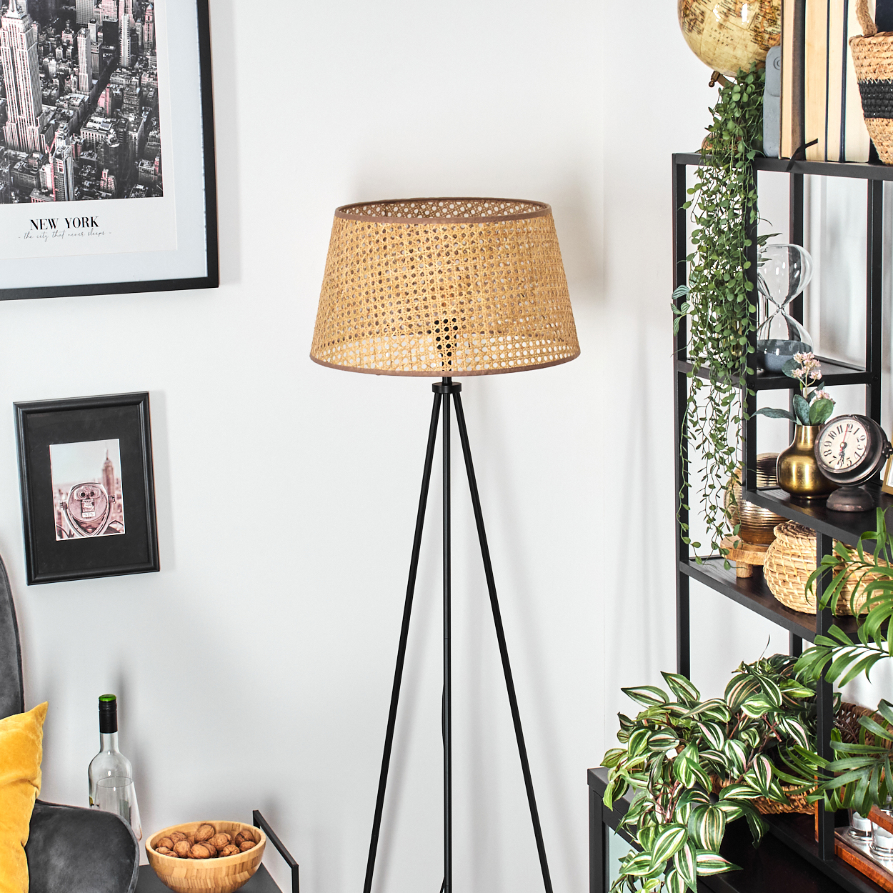 Dreibein-Stehlampe mit gewebtem Schirm. Hintergrund: Kunst, Regal und Pflanzen.