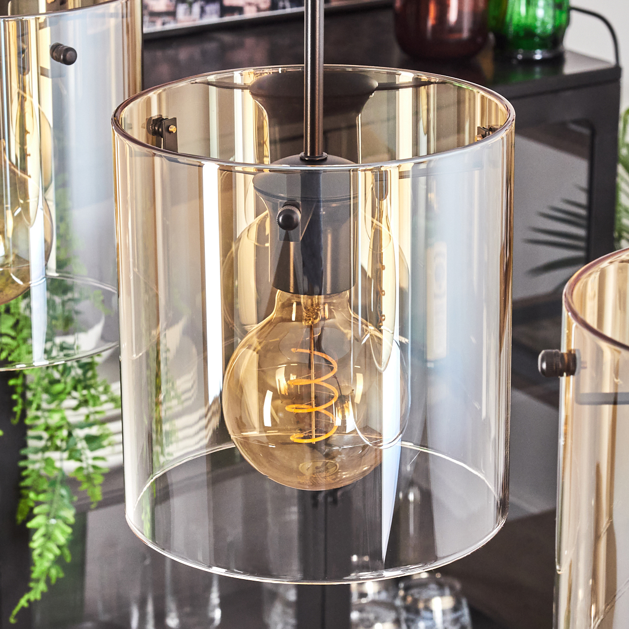 Nahaufnahme einer Pendelleuchte mit bernsteinfarbenem Glasschirm und Edison-Glühbirne. Schwarzer Hintergrund.