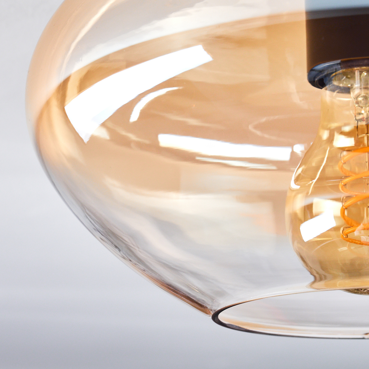 Eine Nahaufnahme eines durchsichtigen, bernsteinfarbenen Glasschirms mit einer sichtbaren, spiralförmigen Glühbirne darin.