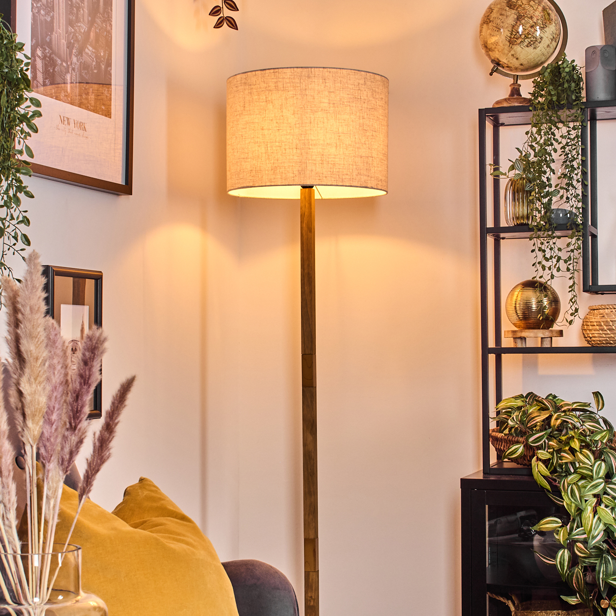 Eine Stehlampe mit beigem Lampenschirm, Holzständer und einem New York Bild im Hintergrund.