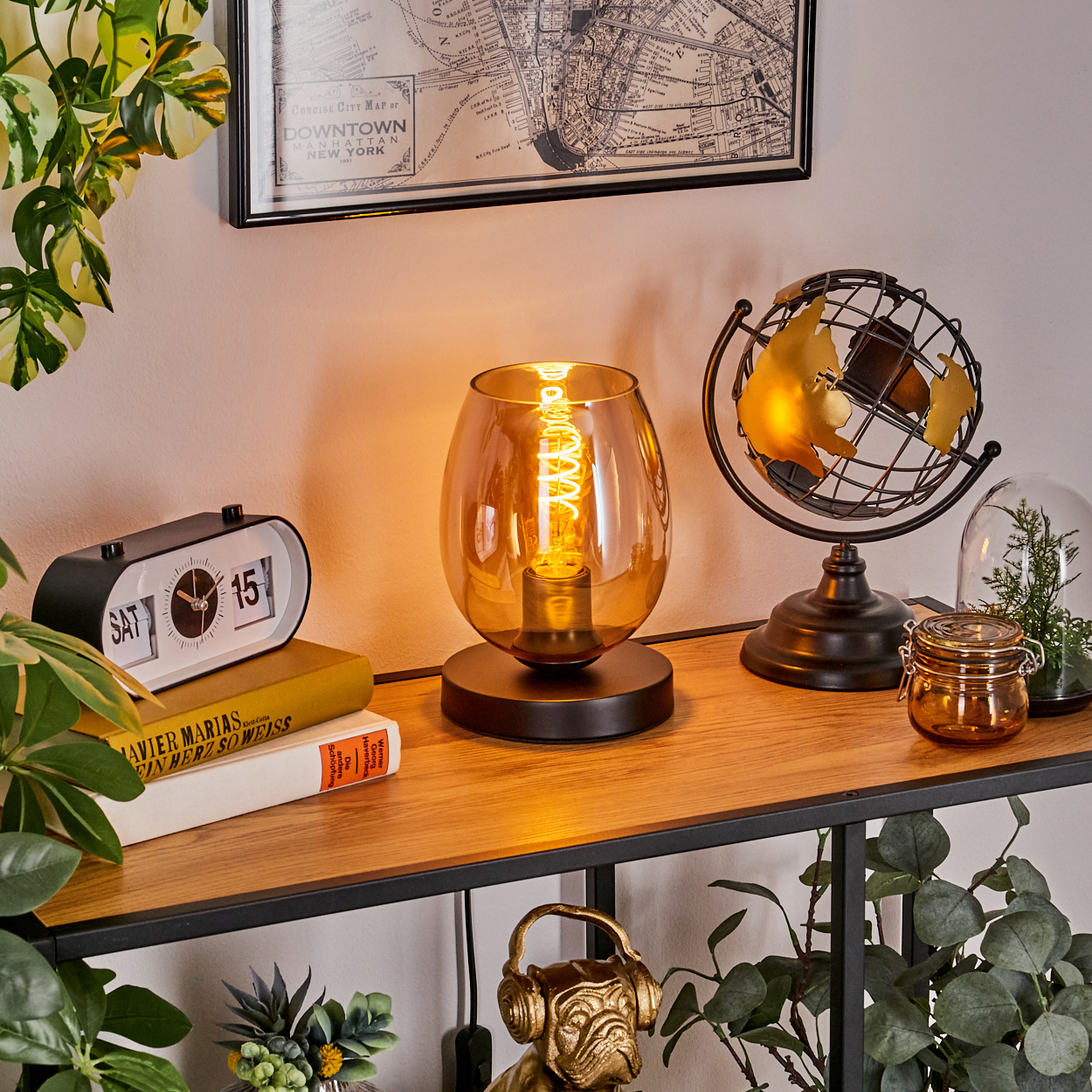 Eine Tischlampe mit bernsteinfarbenem Glasschirm, einer Spirallampe und Dekoration auf einem Regal im Hintergrund.