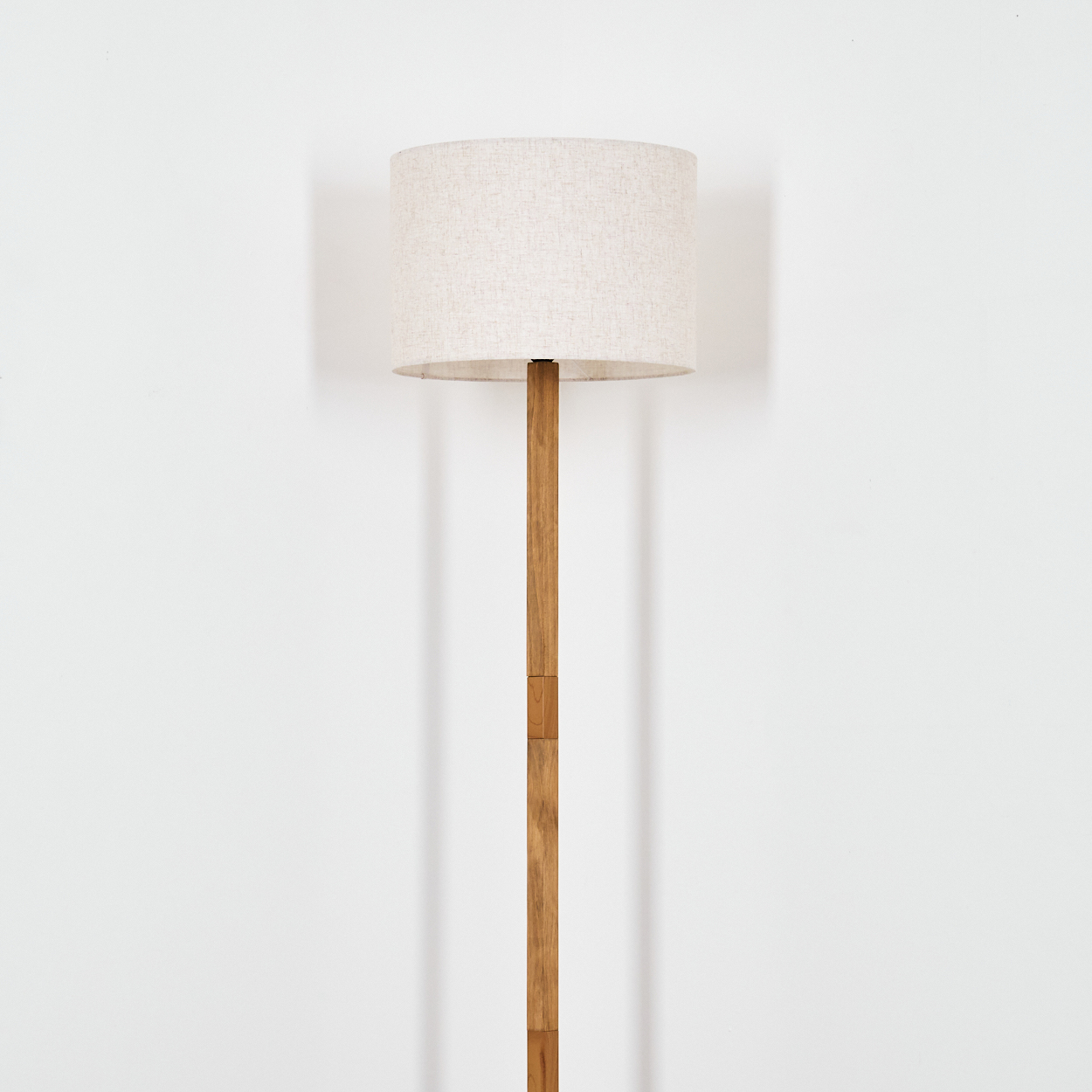 Eine Stehlampe aus Holz mit beigem Lampenschirm. Der Hintergrund ist eine weiße Wand.