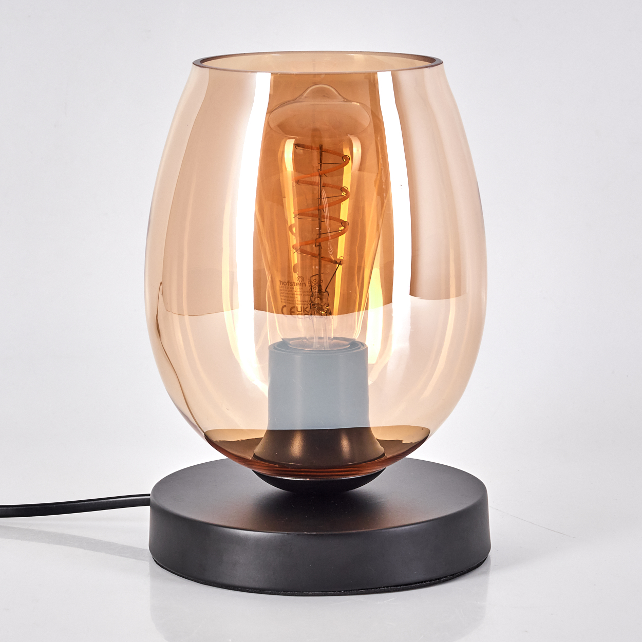 Eine Tischlampe mit bernsteinfarbenem Glasschirm, schwarzem Sockel und sichtbarer Spirallampe.
