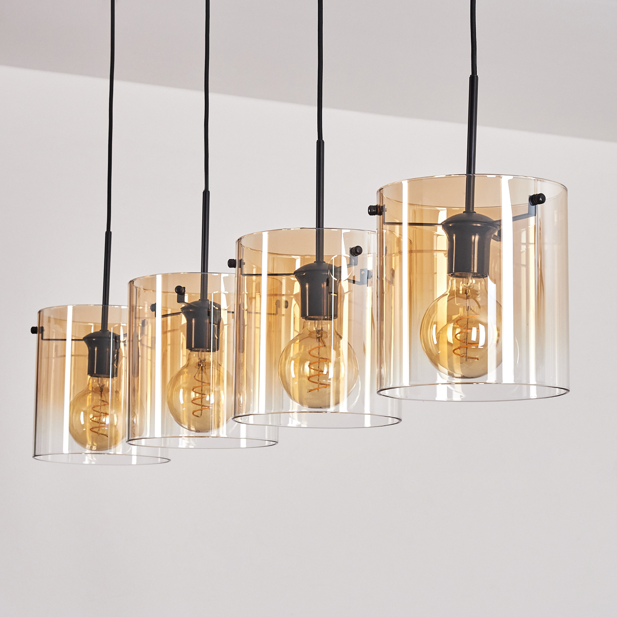 Vier Pendelleuchten mit bernsteinfarbenen Glasschirmen und Edison-Glühbirnen. Schwarze Kabel. Weißer Hintergrund.
