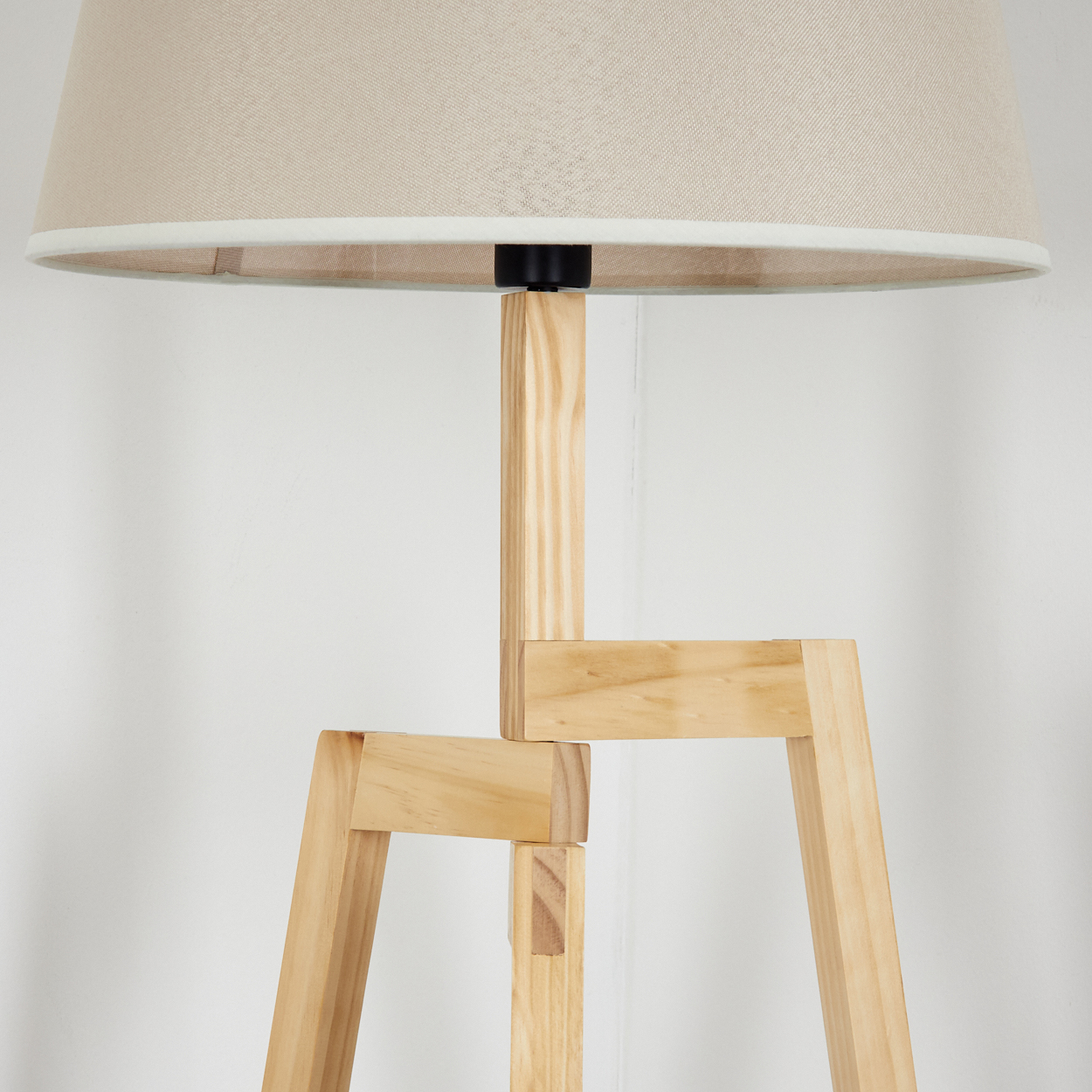 Nahaufnahme eines hölzernen Stativlampenfußes mit beigem Lampenschirm. Die Lampe ist unbeleuchtet.