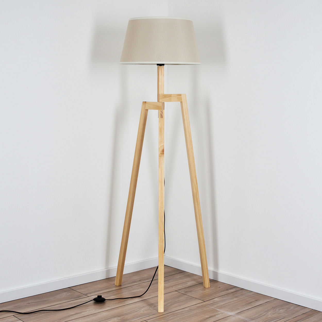 Holz-Stehlampe mit beigem Lampenschirm, die in einer Ecke mit weißen Wänden steht.