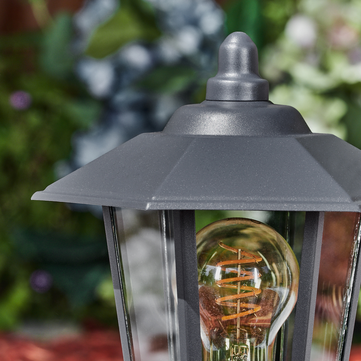 Nahaufnahme einer Außenlampe mit einer Vintage-Glühbirne. Die Lampe hat einen grauen Rahmen. Der Hintergrund ist unscharf.