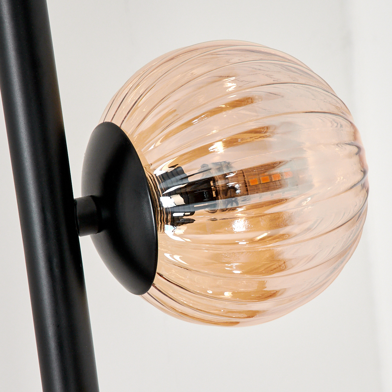 Nahaufnahme einer bernsteinfarbenen Glaskugel mit schwarzem Stiel, Teil einer Lampe.