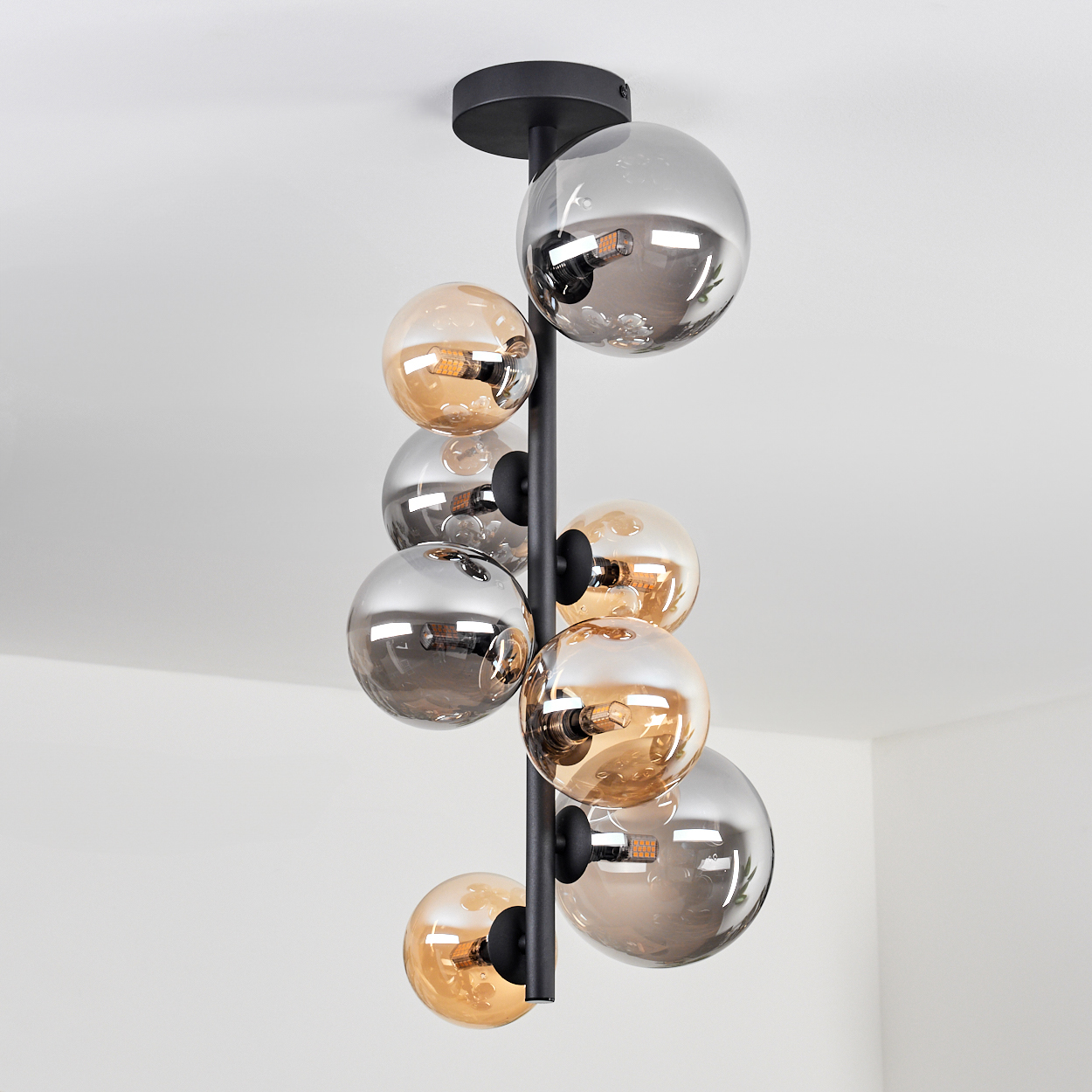 Deckenlampe mit Glaskugeln, schwarzer Rahmen. Die Glühbirnen sind an. Weißer Hintergrund.