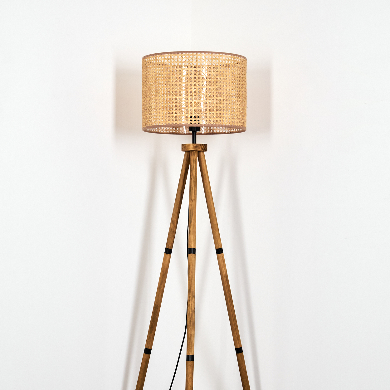 Stehlampe auf Holzbeinen, heller Schirm. Weißer Hintergrund. Die Lampe ist an.