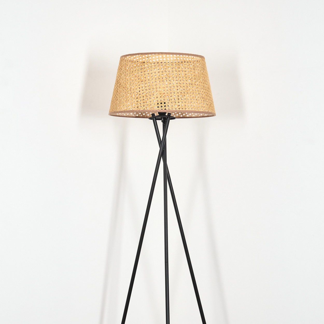 Eine Stehlampe mit einem gewebten Lampenschirm. Der Sockel ist schwarz, der Hintergrund weiß.