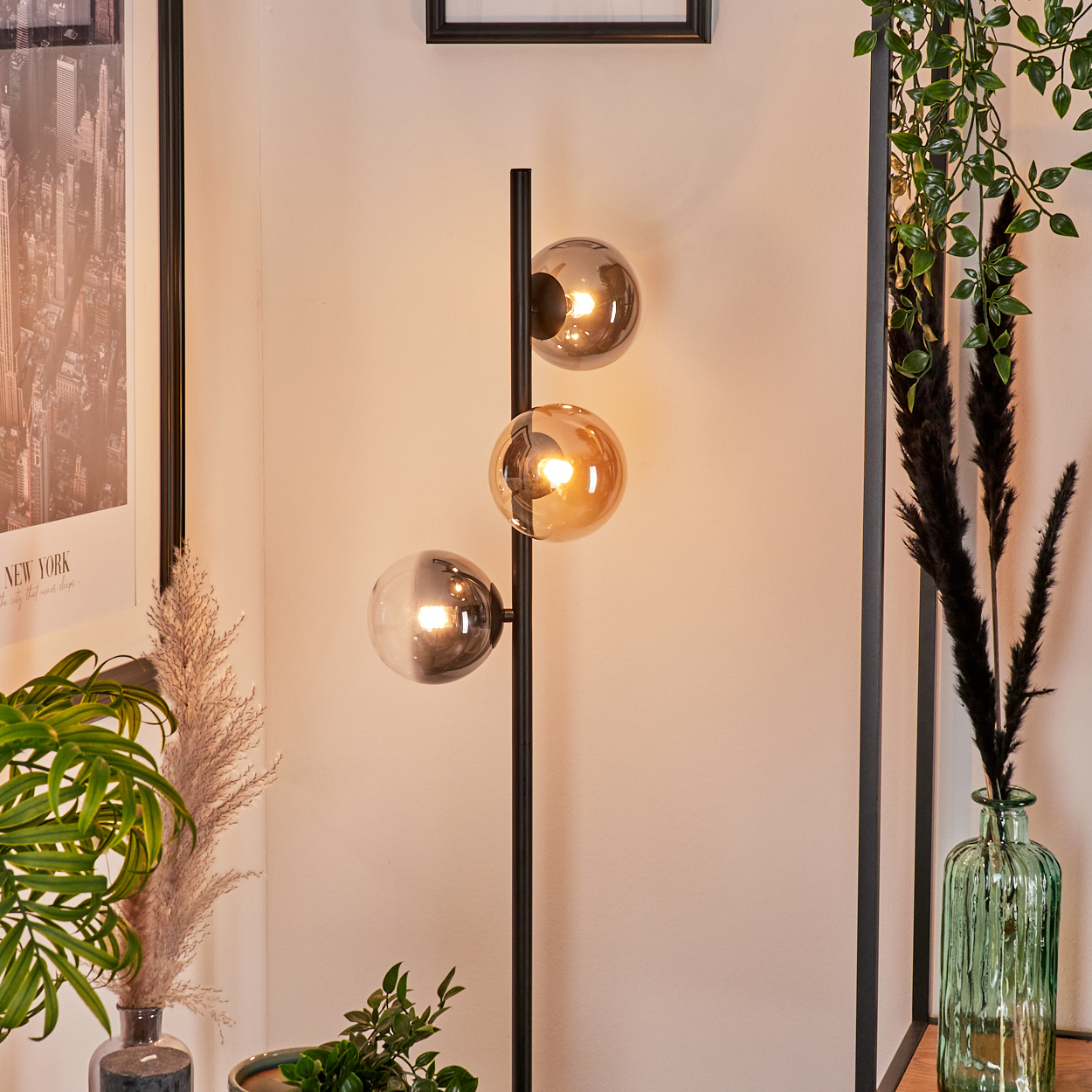 Schwarze Stehlampe mit drei Glas-Kugelschirmen in einem Raum mit Pflanzen und einem New York Poster.