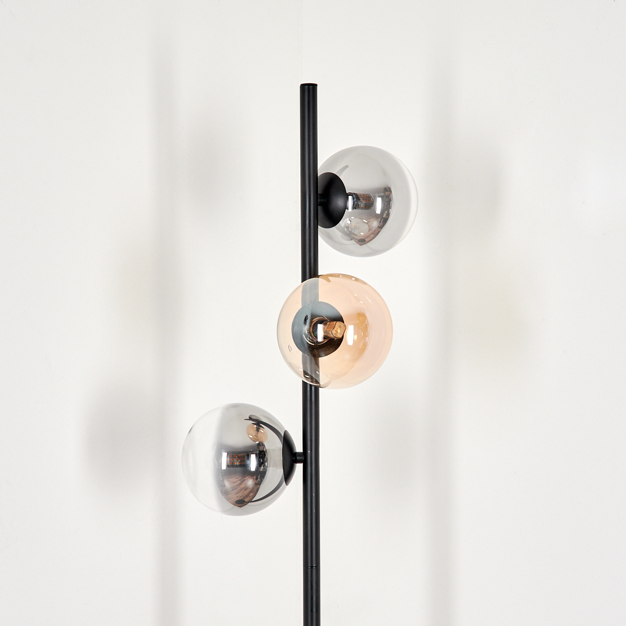 Schwarze Stehlampe mit drei Kugelschirmen, zwei silbernen, einem bernsteinfarbenen, vor weißem Hintergrund.