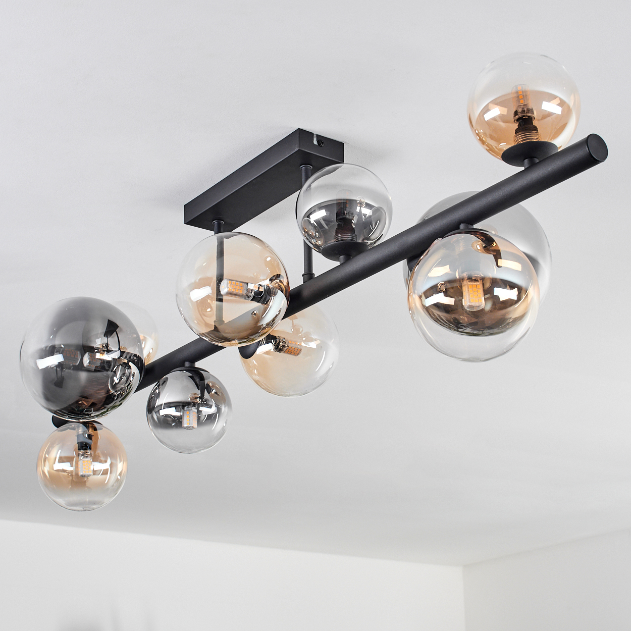 Deckenleuchte mit Kugelschirmen. Schwarze Halterung mit bernsteinfarbenen und silbernen Glaskugeln. Weiße Decke.