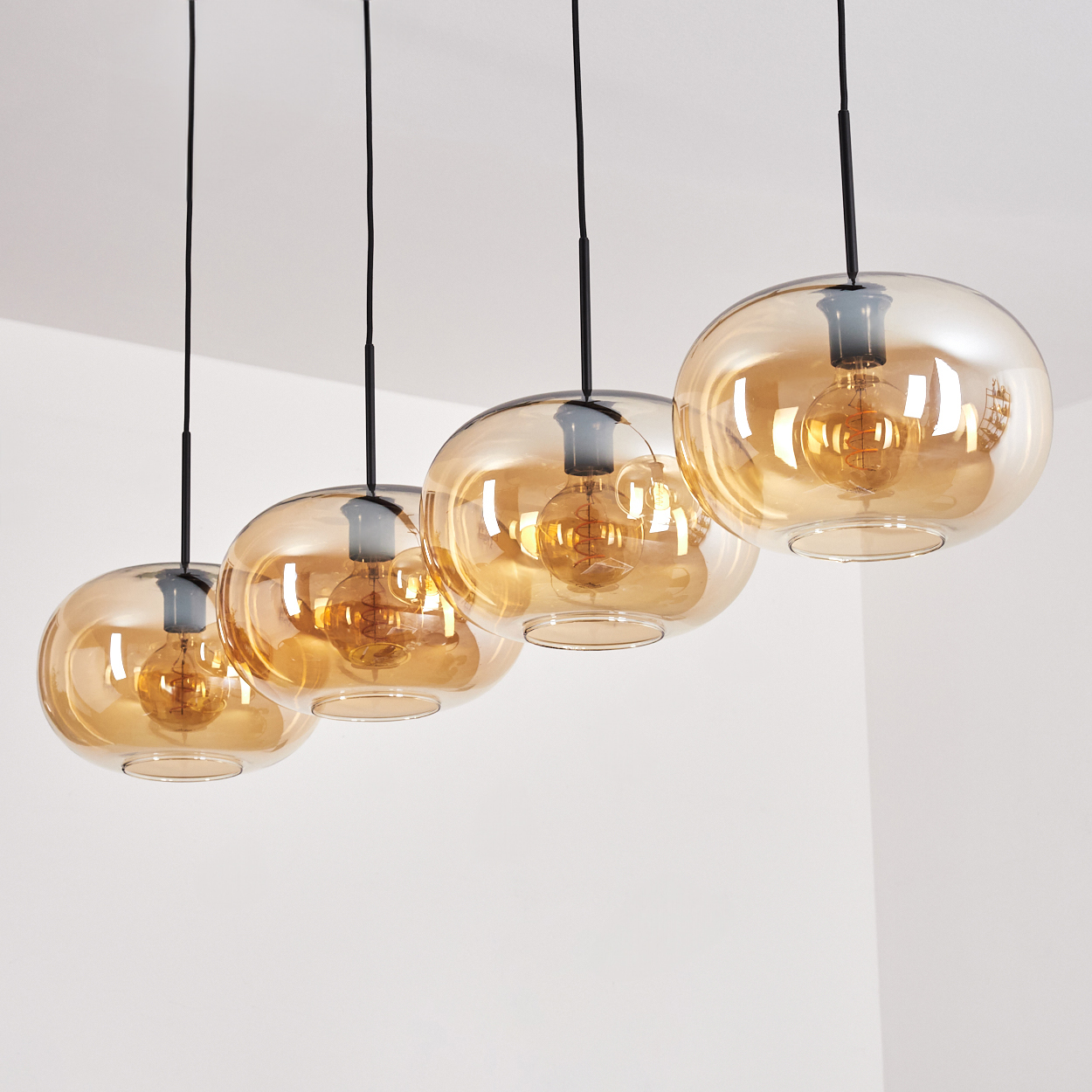 Vier Pendelleuchten mit bernsteinfarbenen Glaskugeln. Die Lampen hängen von einer weißen Decke.