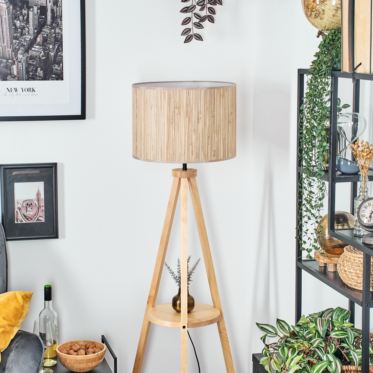 Eine hölzerne Stativ-Stehlampe mit gewebtem Lampenschirm. Die Lampe befindet sich in einem Raum mit Kunst und Pflanzen.