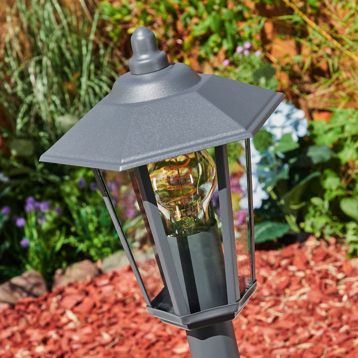 Nahaufnahme einer Außenlampe mit einer leuchtenden Glühbirne. Die Lampe ist grau und der Hintergrund ist grün.