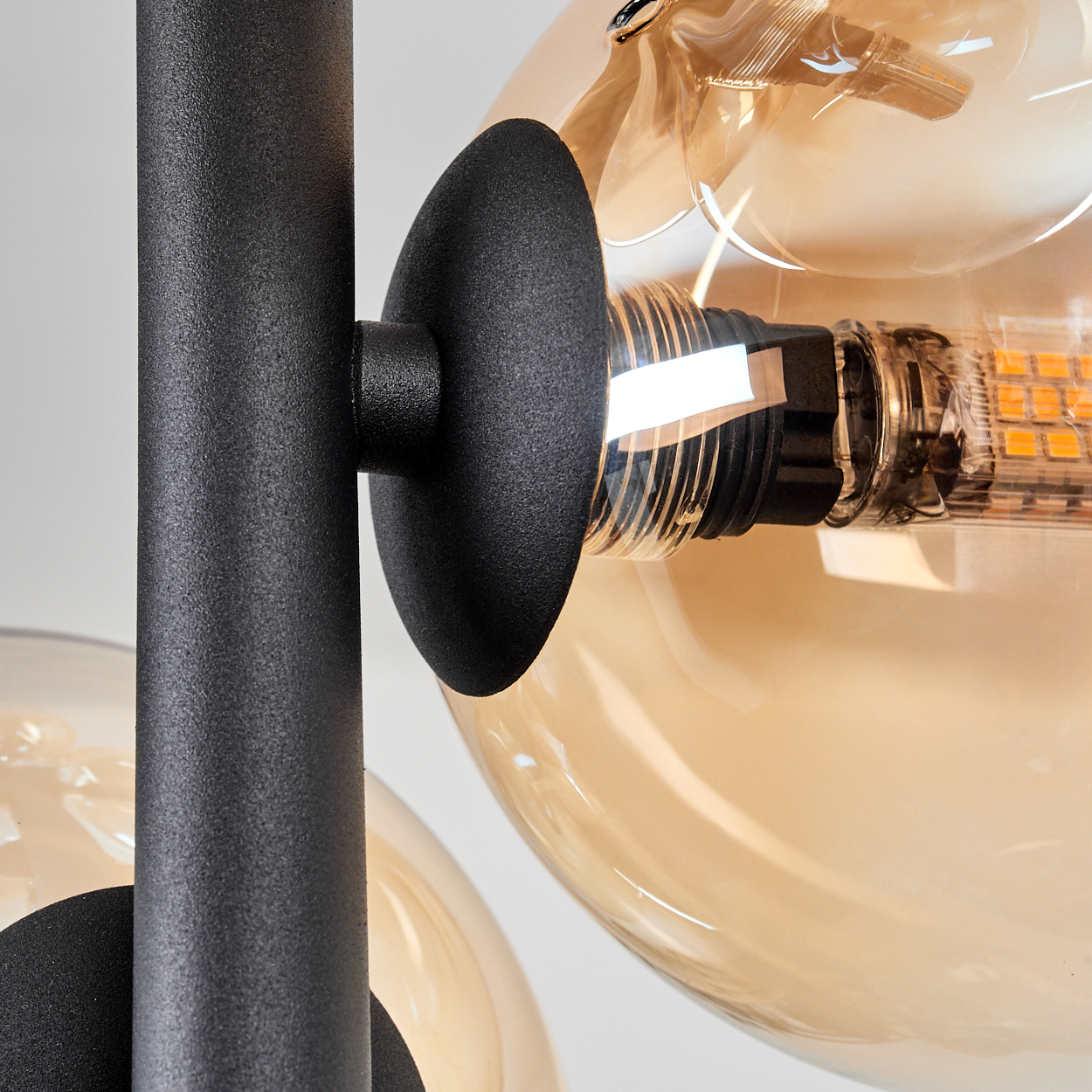 Nahaufnahme einer schwarzen Lampe mit einer gelben Glühbirne. Die Glühbirne befindet sich in einem durchsichtigen Glaskugel.