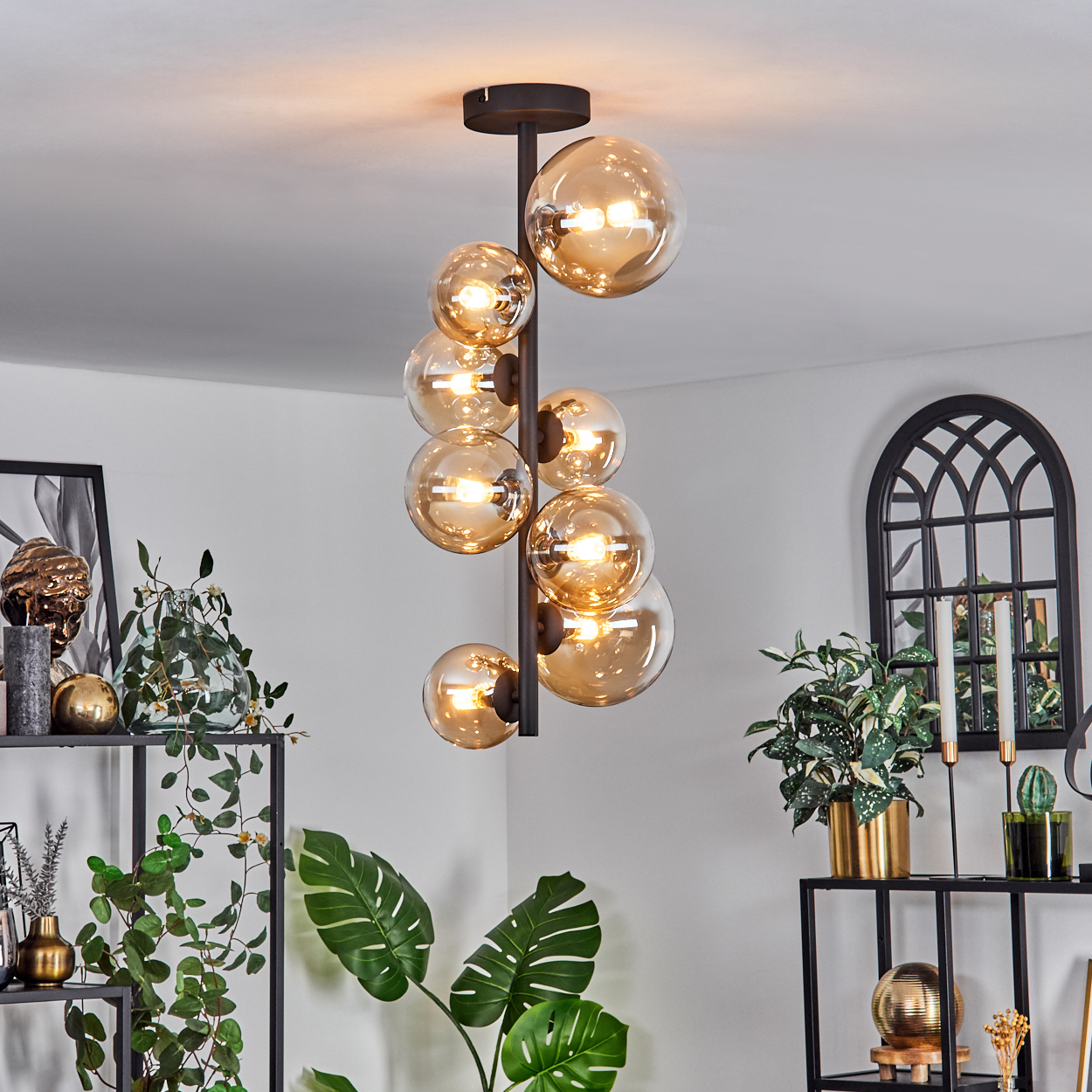 Hängende schwarze Lampe mit mehreren orangefarbenen Glaskugeln. Innenszene mit Pflanzen und Dekoration.