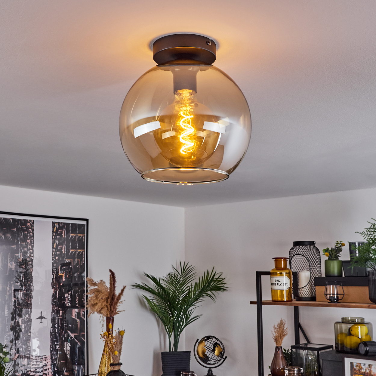 Nahaufnahme einer Deckenlampe mit orangefarbenem Globus und heller Glühbirne. Raum mit Deko.