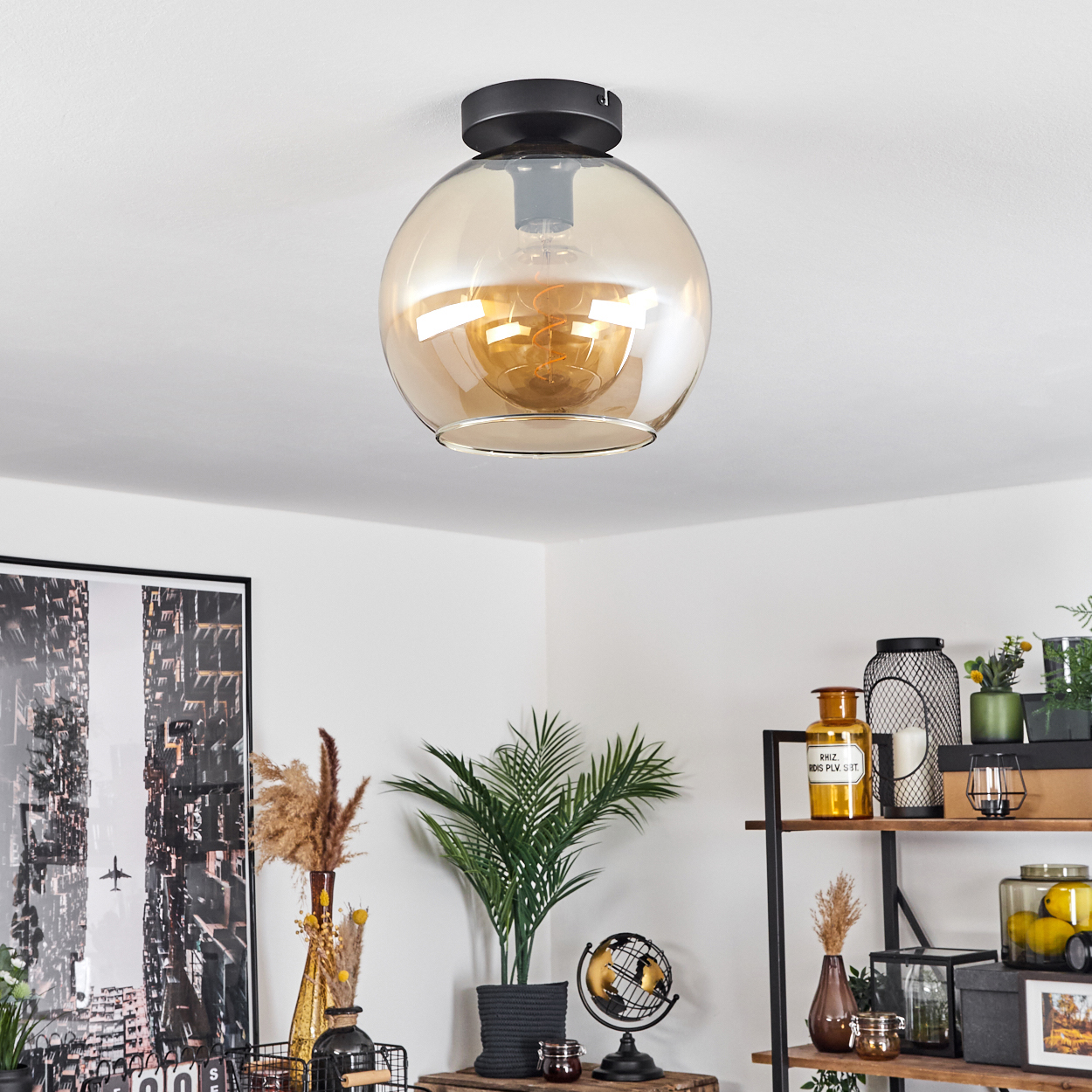 Eine Deckenleuchte mit einer bernsteinfarbenen Kugelleuchte. Das Bild zeigt die Lampe in einem Raum mit einem New York-Gemälde.