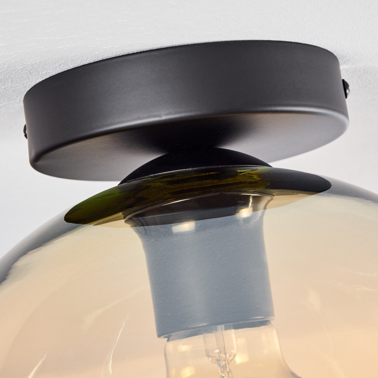 Nahaufnahme einer Deckenlampe mit orangefarbenem Glas. Die Glühbirne ist sichtbar.