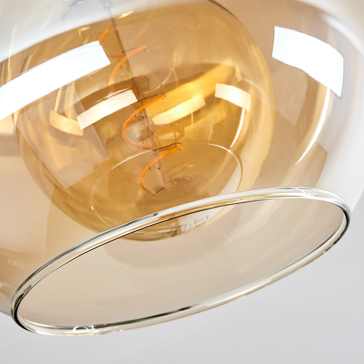 Nahaufnahme einer Glühbirne mit Glasschirm. Der Schirm ist bernsteinfarben, die Glühbirne hat einen Spiralglühfaden.