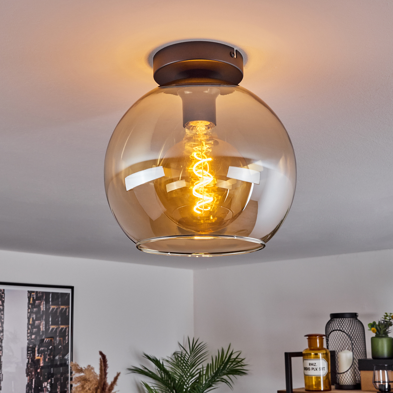 Deckenleuchte mit bernsteinfarbenem Glaskugel. Das Licht ist an und beleuchtet die Glühbirne im Inneren.