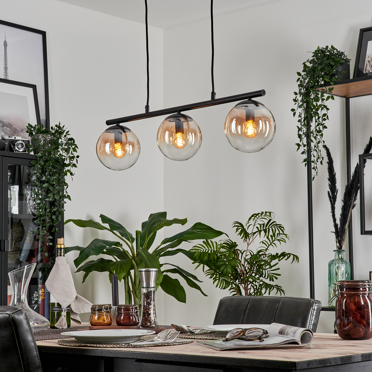 Ein Esszimmer mit einem Holztisch, drei bernsteinfarbenen Glaskugel-Pendelleuchten und einer Vielzahl von Dekorationen.