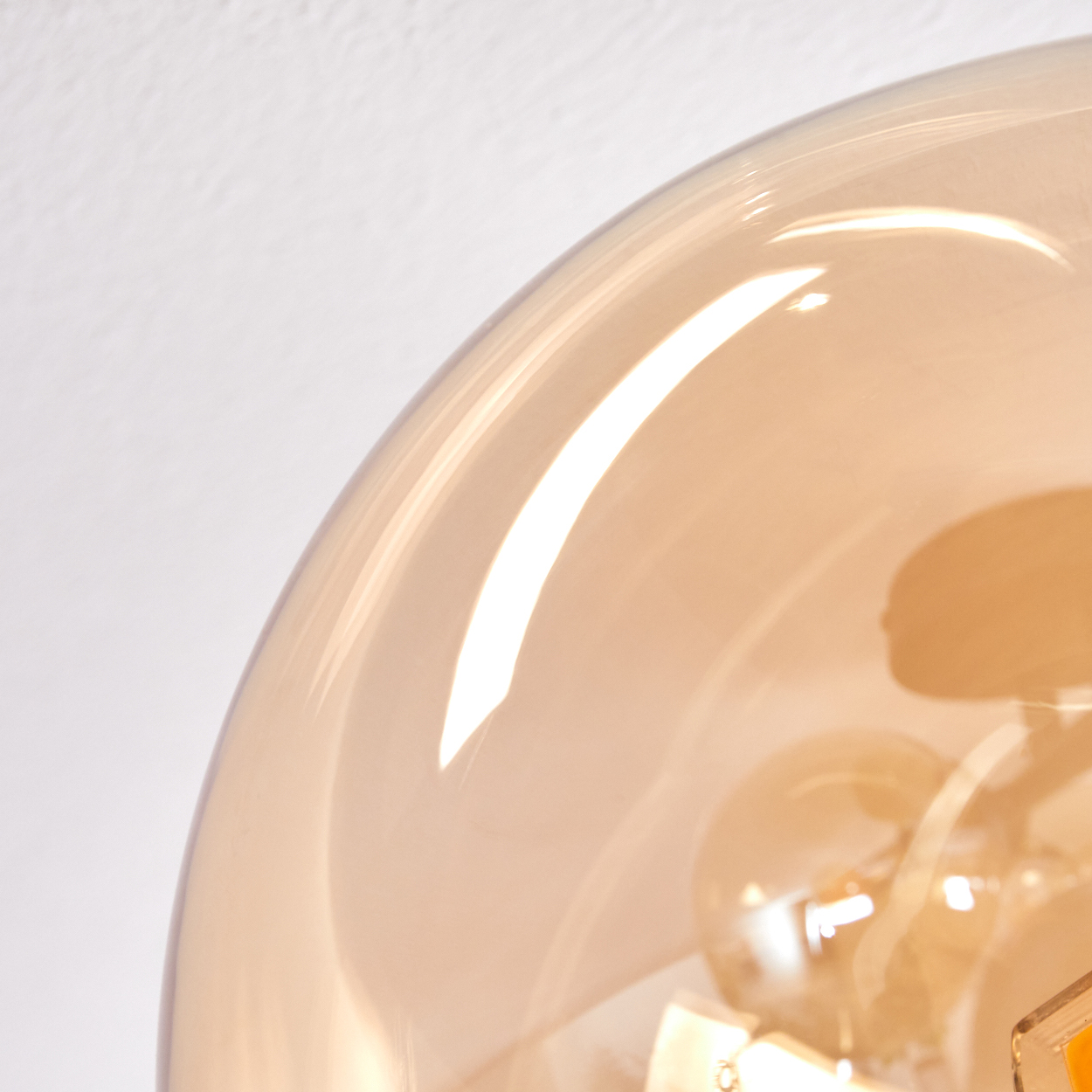 Nahaufnahme einer Glaskugel-Leuchte. Das Glas ist bernsteinfarben, der Hintergrund ist weiß.