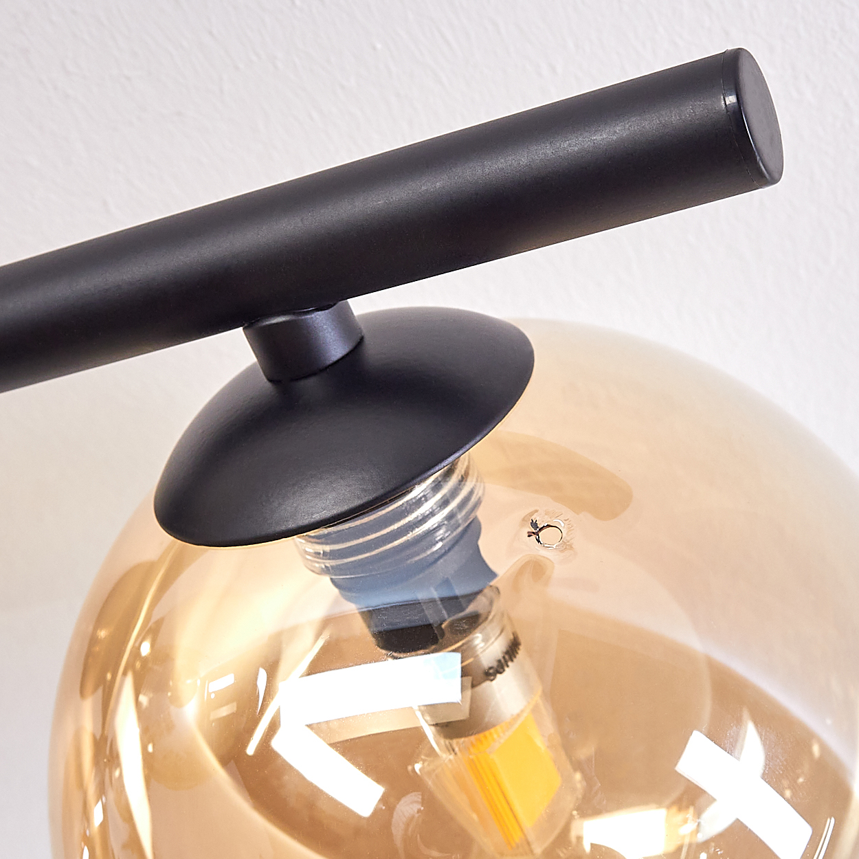 Nahaufnahme einer Lampe und Glühbirne. Die Glühbirne befindet sich in einer bernsteinfarbenen Glaskugel.