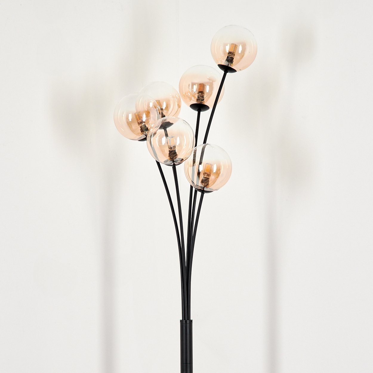 Stehlampe mit 6 bernsteinfarbenen Glaskugeln vor einer weißen Wand. Die Lampe ist schwarz.