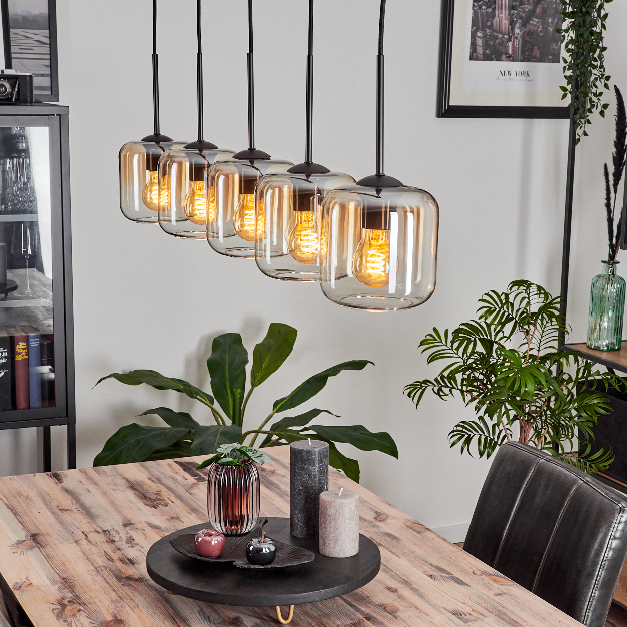 Esszimmer mit Holztisch, 6 Pendelleuchten, Pflanzen und Dekorationsartikeln.