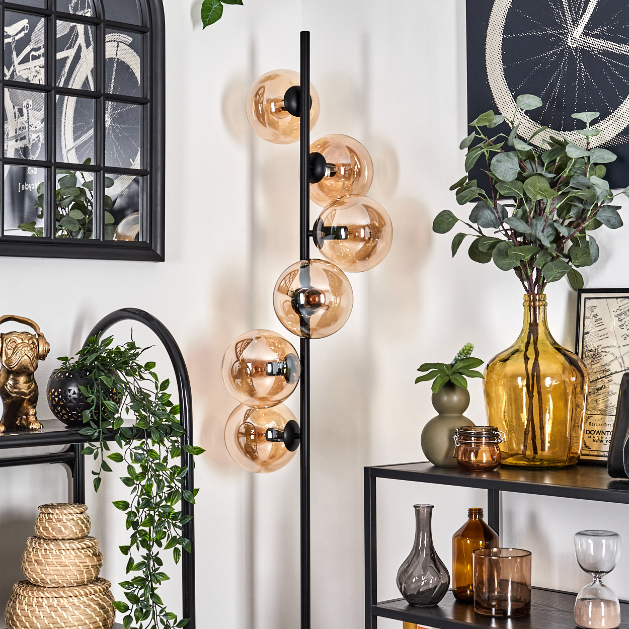 Eine schwarze Stehlampe mit bernsteinfarbenen Glaskugellampen, neben einem Regal mit Dekorationen.