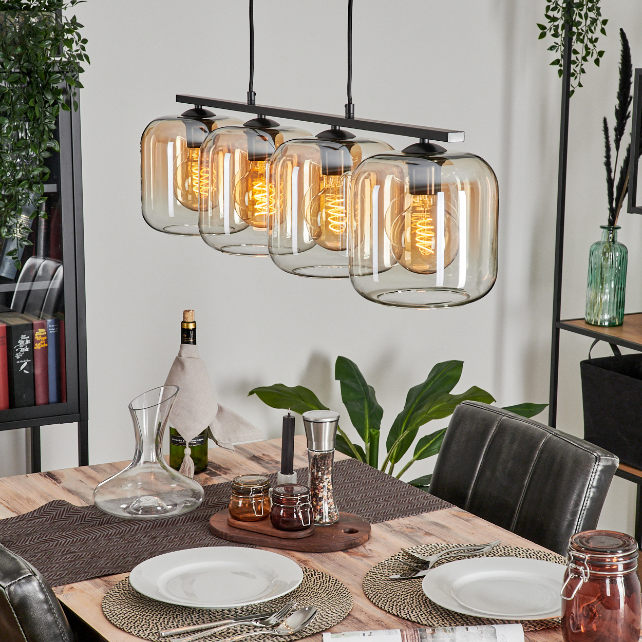 Esstisch mit Hängelampen. Die Lampen sind aus Klarglas mit bernsteinfarbenen Glühbirnen. Der Tisch ist gedeckt.