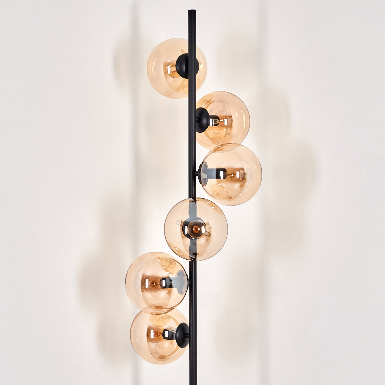 Stehlampe mit bernsteinfarbenen Glaskugeln, schwarzem Rahmen und sichtbaren Glühbirnen.