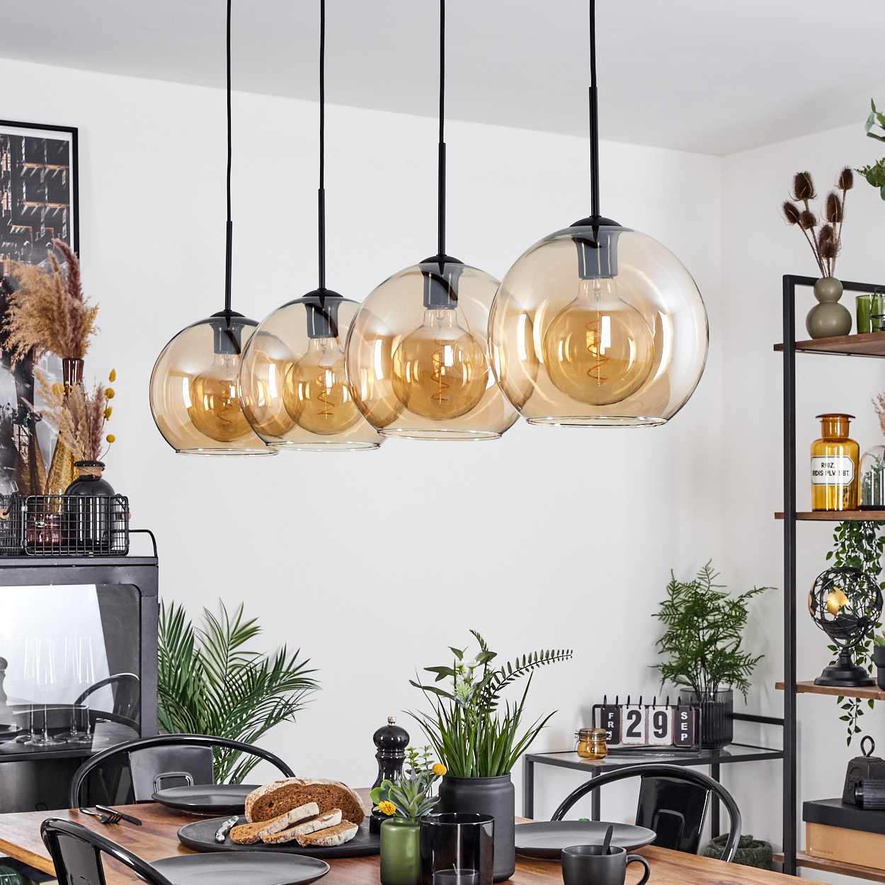 Esszimmer mit Hängelampen. Die Lampen sind Glaskugeln mit bernsteinfarbenen Glühbirnen. Tisch ist gedeckt.
