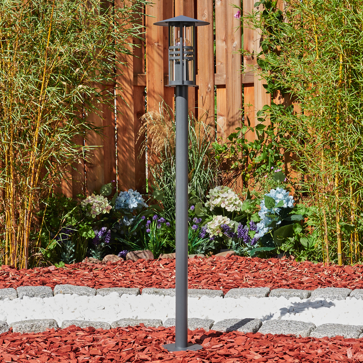 Außenszene mit einer Lampe. Die Lampe hat einen schwarzen Pfahl und der Hintergrund ist ein Garten.