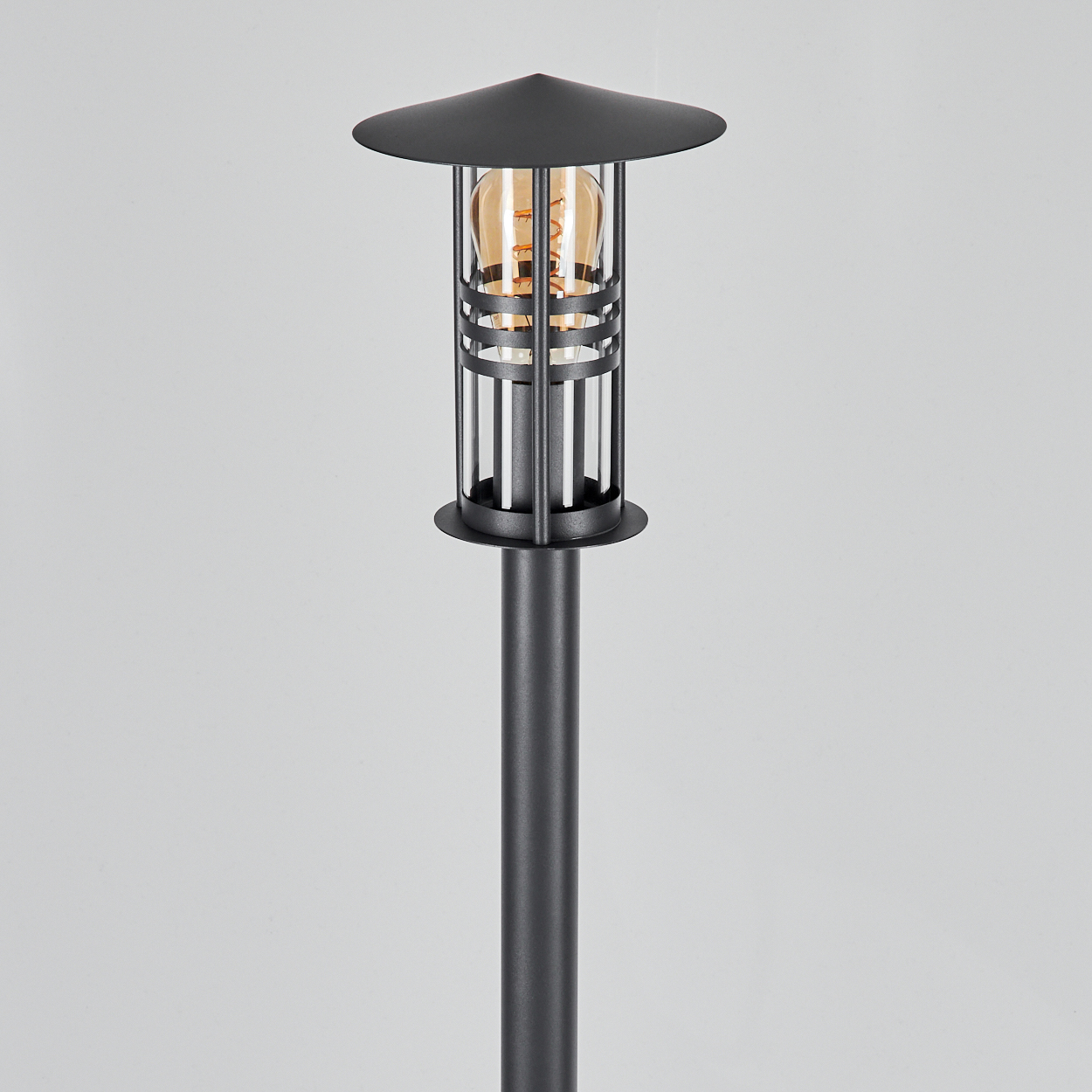 Außenlampe. Die Lampe ist schwarz und hat einen Käfig um die bernsteinfarbene Glühbirne.
